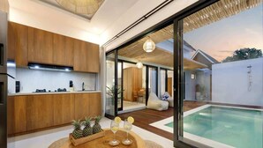 A modern kitchen with wooden cabinets, a dining area with a wooden table, and a view of a swimming pool.