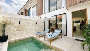 A modern house with a swimming pool, two lounge chairs, and a stone wall.