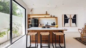 A modern kitchen with a large island, bar stools, and a view of greenery outside.