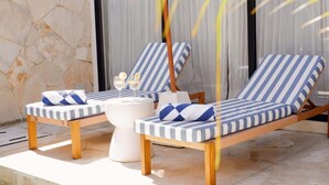 Two lounge chairs with striped cushions, a white side table, and a glass of wine.