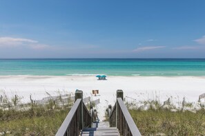 A wooden boardwalk leading to a beach with a blue umbrella and chairs.