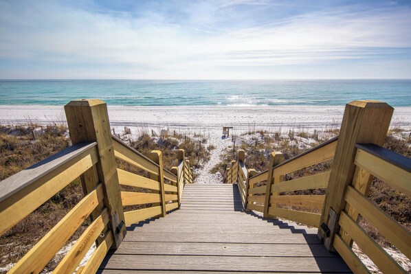 Una escalera de madera que da a una playa, con vista clara al océano.