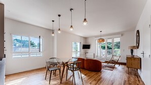 Una habitación amplia con piso de madera, una mesa de comedor con sillas, un sofá y un televisor montado en la pared.