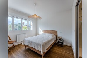Une chambre avec un lit en bois, une fenêtre, un radiateur et une chaise.