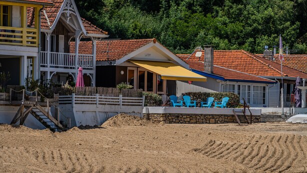 Una propiedad frente a la playa con una estructura de madera, un muro de piedra y sillas azules.