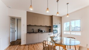 Una cocina moderna con suelo de madera, una mesa de comedor de cristal e iluminación colgante.