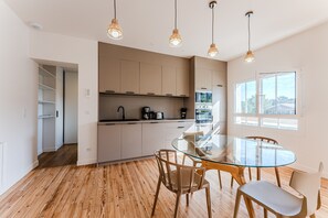 A modern kitchen with wooden flooring, a glass dining table, and pendant lighting.