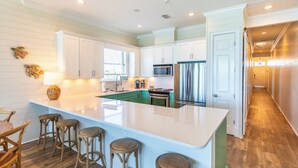 A spacious kitchen with white cabinets, a large island with stools, a microwave, and a refrigerator. - Journeys End 205 - Welcome to your coastal escape! Gulf Front! Private Beach! (Santa Rosa Beach)