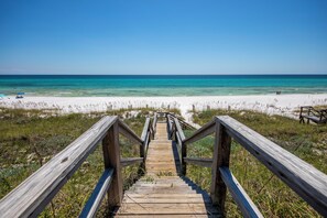Une promenade en bois menant à une plage où l’eau est d’un bleu cristallin et le sable, d’un blanc éclatant.