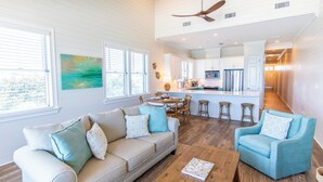 A spacious living room with a sofa, armchairs, and a coffee table. A kitchen with white cabinets and a dining area with a table and chairs is visible in the background. - Journeys End 205 - Welcome to your coastal escape! Gulf Front! Private Beach! (Santa Rosa Beach)