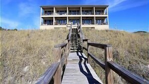 A wooden boardwalk leading to a building with multiple balconies, situated on a grassy hill. - Journeys End 205 - Welcome to your coastal escape! Gulf Front! Private Beach! (Santa Rosa Beach)