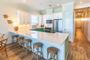 A spacious kitchen with white cabinets, a large island with stools, a microwave, and a refrigerator. - Journeys End 205 - Welcome to your coastal escape! Gulf Front! Private Beach! (Santa Rosa Beach)