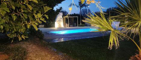 Una piscina con un camino de piedra que la conduce, rodeada de follaje y un pabellón.