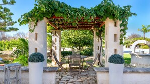 Un chemin de pierres mène à une pergola sous laquelle se trouvent une table et des chaises.