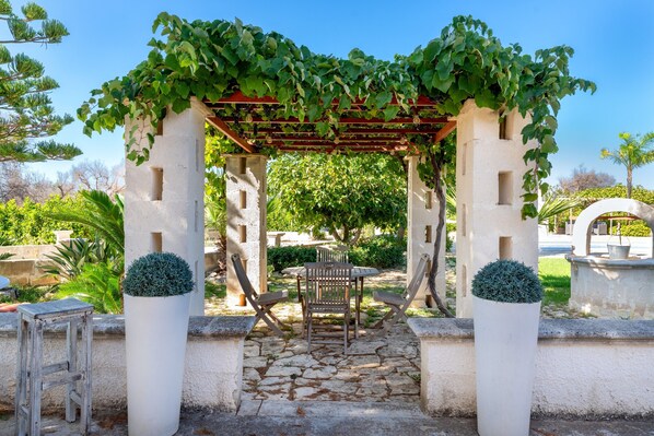 A stone pathway leading to a pergola with a table and chairs underneath.