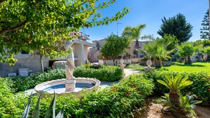 Un jardin agrémenté d’une fontaine, de différentes plantes et d’un bâtiment à la façade en pierre.