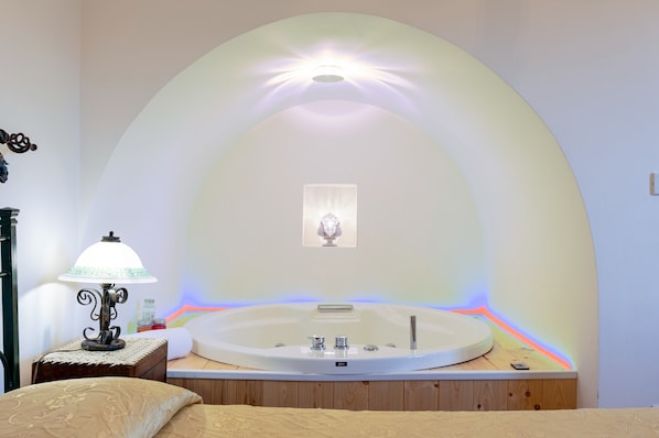 Une salle de bain avec une baignoire sur pieds, un luminaire fixé au mur et une petite table de chevet avec une lampe.