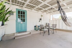 Un espace extérieur abrité, doté d’une porte turquoise, d’une table avec des chaises et d’un hamac.