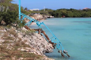 Un escalier métallique bleu qui descend vers une étendue d’eau, entouré d’un terrain rocheux et d’une végétation clairsemée.