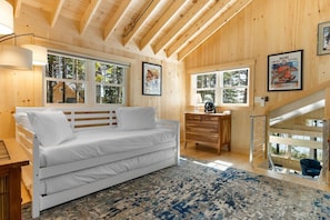 L'intérieur d'une cabane en bois, avec un lit, une commode et un escalier.