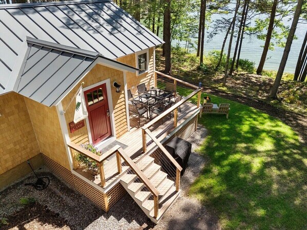 Une cabane avec une terrasse, une porte rouge et une vue sur le lac.