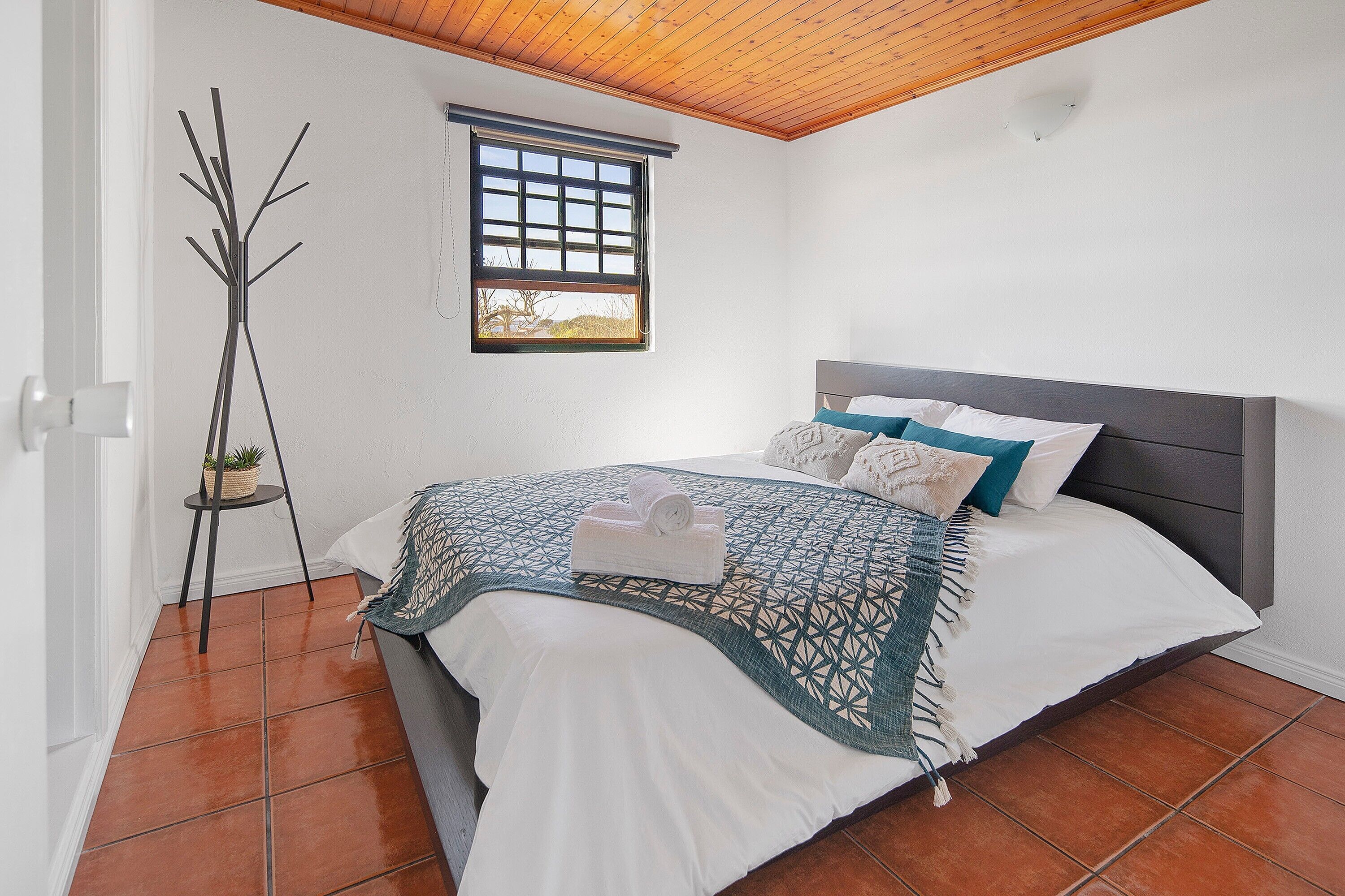 A bedroom with a bed, a window, a plant, and a floor lamp.