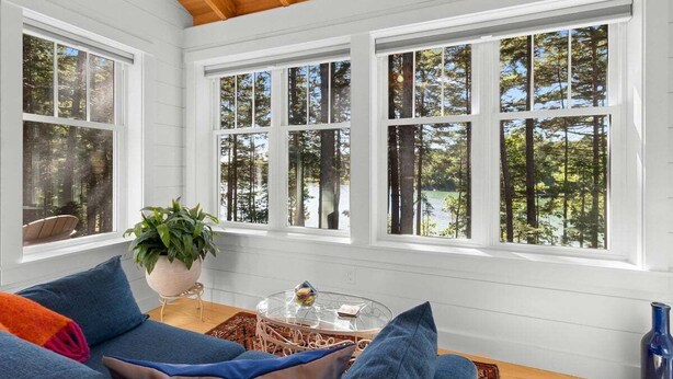 A room with a wooden ceiling, white walls, and large windows with a forest view. - Lindquist Cottage | Waterfront Studio with King Be (Tenants Harbor)