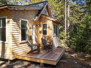 Une cabane en bois avec une terrasse, deux chaises et une table.