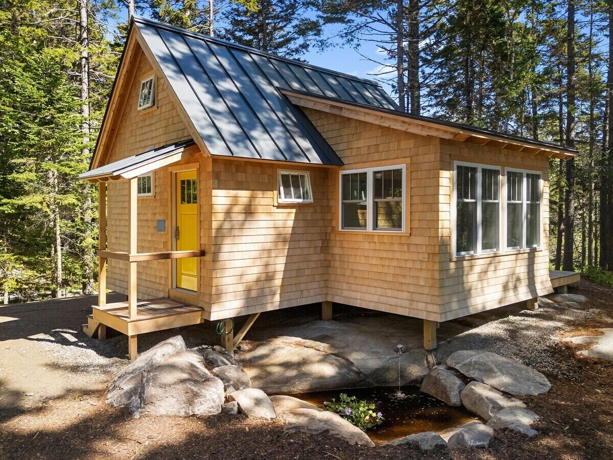 Una cabaña de madera con techo metálico, puerta amarilla y un pequeño porche.