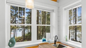 A kitchen with a wooden countertop, a sink, and a window with a view of trees and a body of water. - Lindquist Cottage | Waterfront Studio with King Be (Tenants Harbor)