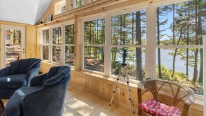 Eine Holzhütte mit großen Fenstern, rustikalem Interieur und Blick auf Wald und See.