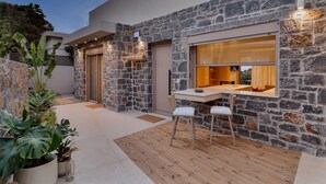 Un patio moderno al aire libre con muros de piedra, un deck de madera y un comedor con dos sillas y una mesa.