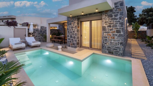 Un área de piscina exterior moderna con sillones de descanso, una pared de piedra y una puerta de cristal que da a un patio.