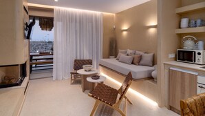 Una sala de estar moderna con un sofá, dos sillones, una mesita, una zona de cocina con microondas y vistas a la ciudad a través de una ventana.