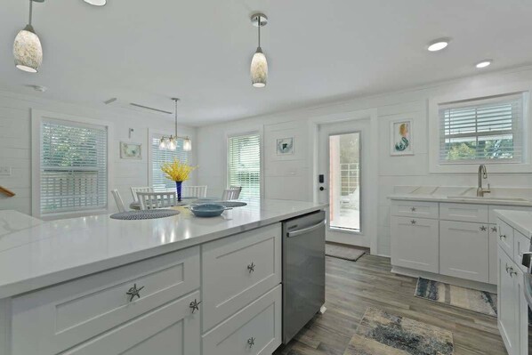 A modern kitchen with white cabinetry, a large island, pendant lights, and a view of the outdoors through the windows.