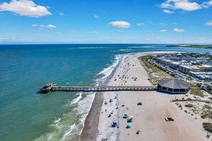 A beach with a pier extending into the ocean, a gazebo, and a row of buildings along the shore.