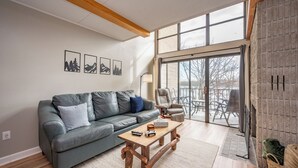 Un salon avec un canapé gris, une table basse en bois et une grande fenêtre.
