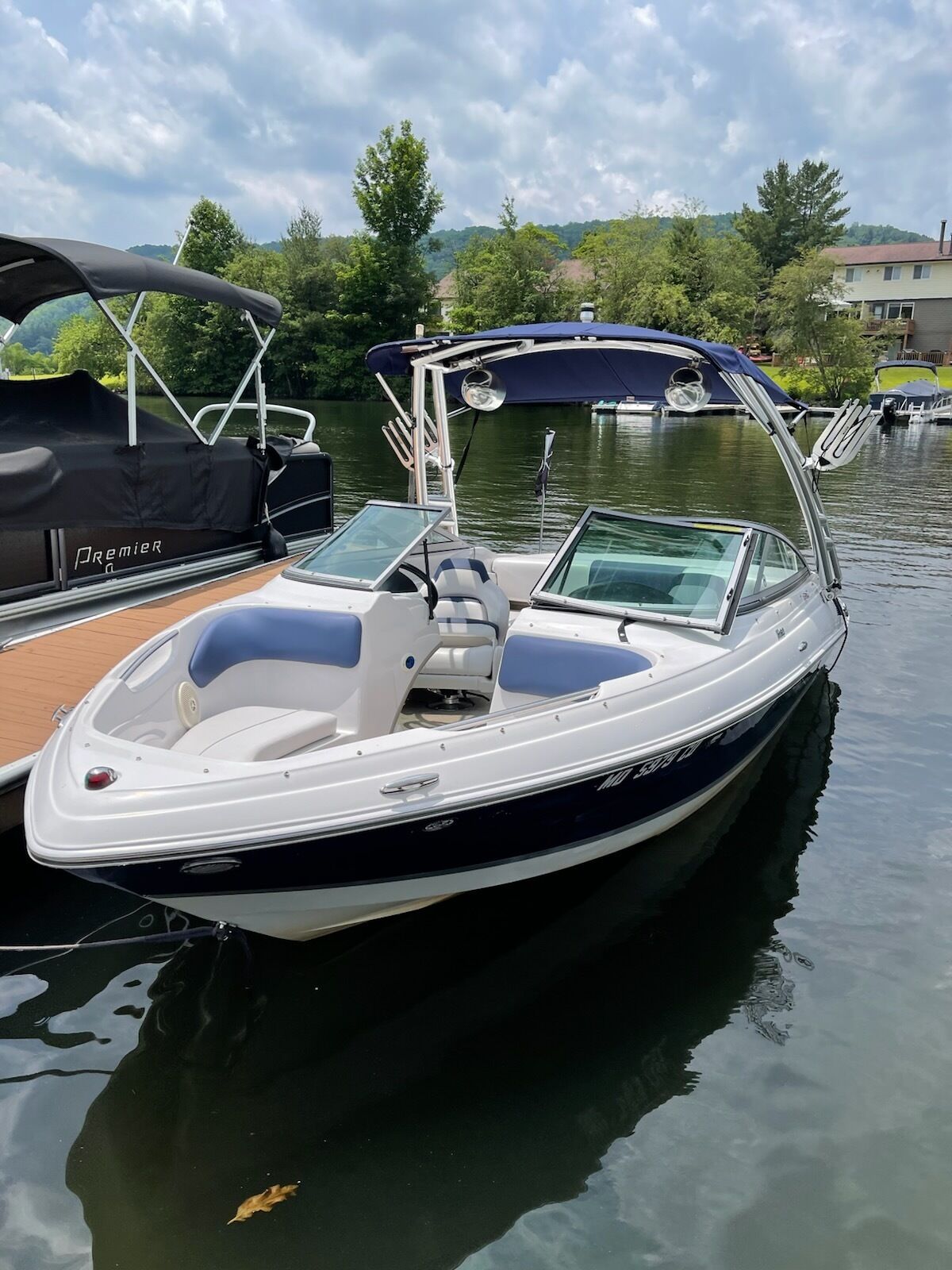 A small, white motorboat with a blue canopy, docked at a calm water body.