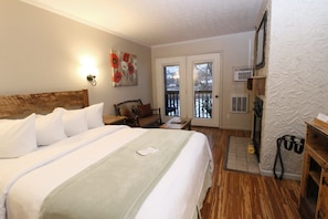 A hotel room with a large bed, a desk, a chair, a small table, a picture on the wall, and a door leading to a balcony.