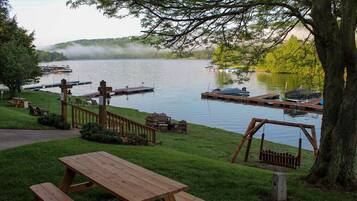Un espace de pique-nique au bord du lac, avec des bancs et des tables en bois, entouré d’une végétation luxuriante et de bateaux amarrés.