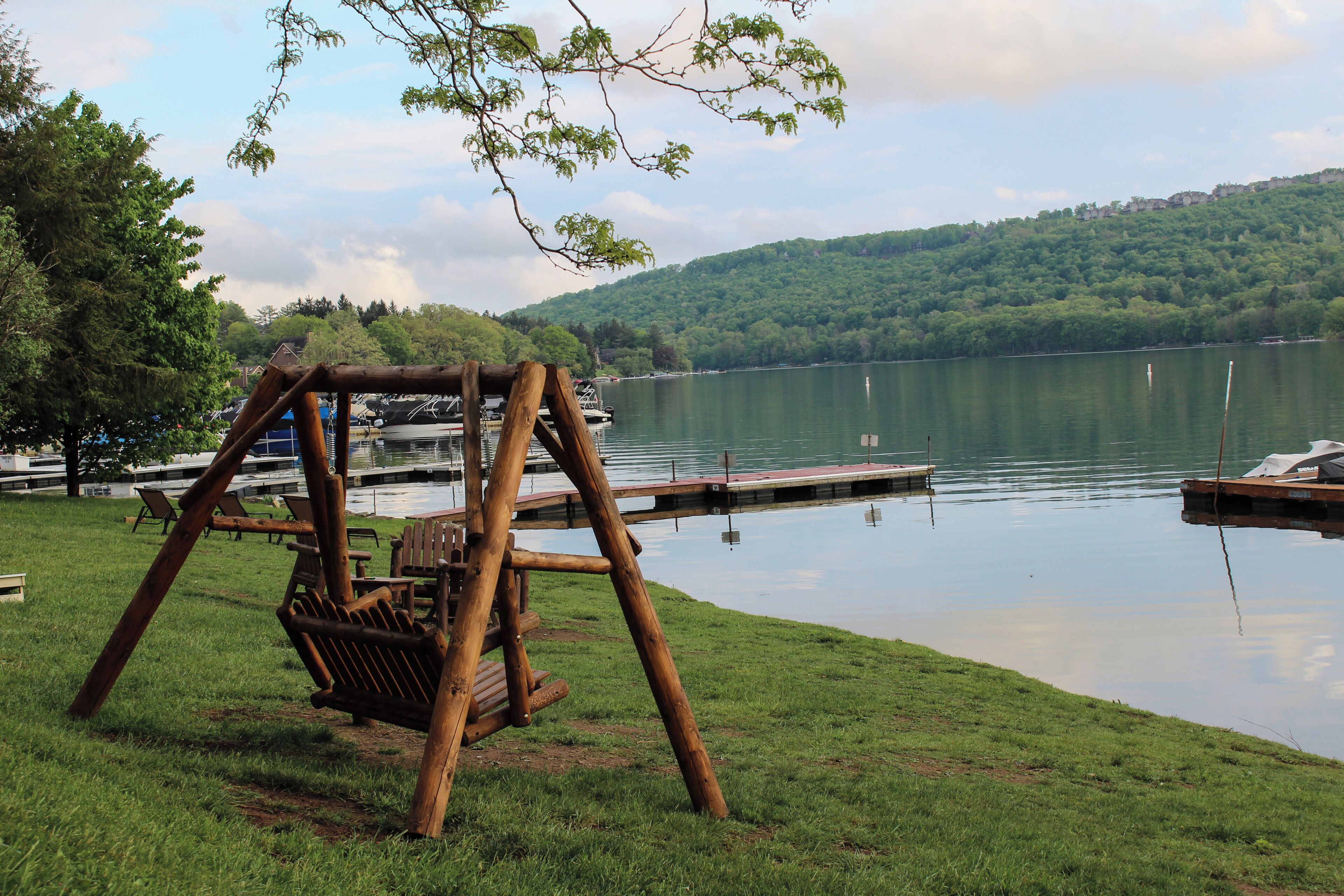 A lakeside setting with a wooden swing set, docked boats, and a grassy area.