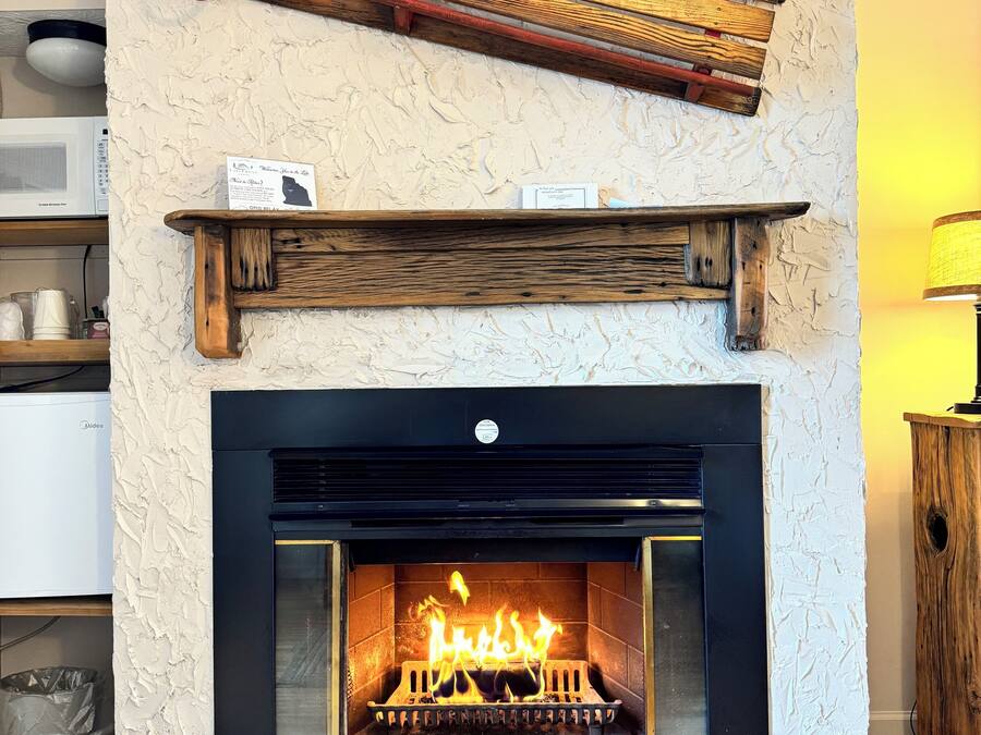 A fireplace with a wooden mantel, a sign above it, and a fire burning inside.