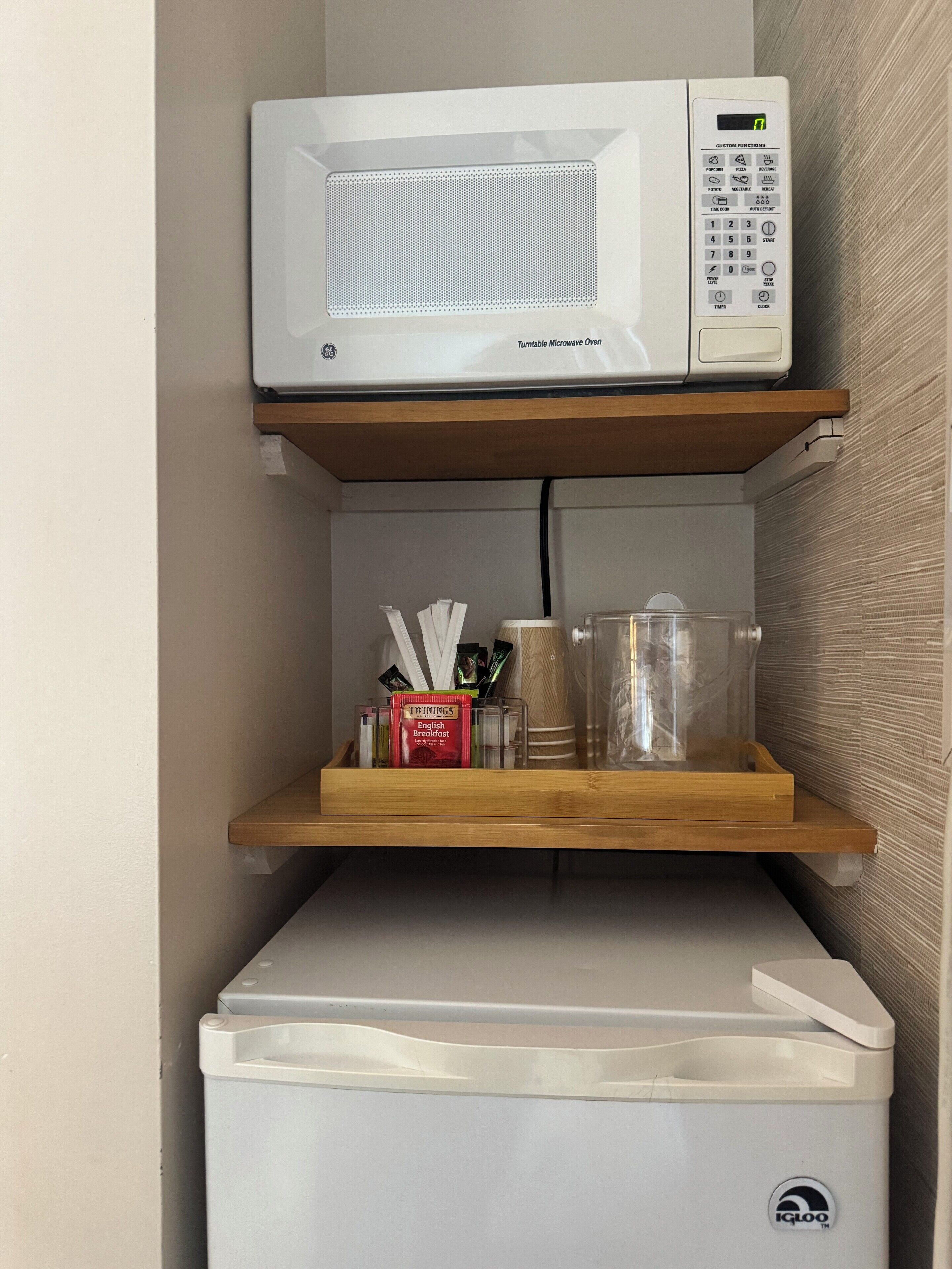 A turntable microwave oven on a shelf above a small refrigerator.
