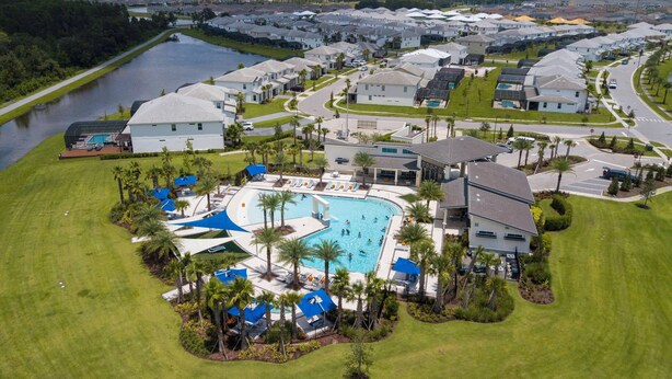 An aerial view of a residential area with a large swimming pool surrounded by houses, palm trees, and a river. - Stunning Mansion 15 ensuites (Kissimmee)