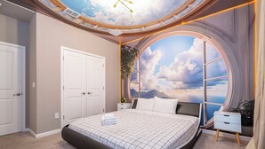 A bedroom with a large bed, a skylight, a view of the sky through a window, and a nightstand with a lamp. - Stunning Mansion 15 ensuites (Kissimmee)