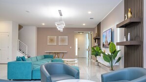 A modern living room with a sectional sofa, two armchairs, a marble coffee table, and a staircase leading to another level. - Stunning Mansion 15 ensuites (Kissimmee)