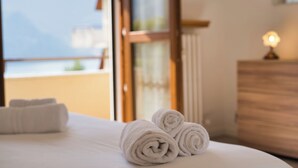Una cama bien hecha con toallas blancas enrolladas y vistas a las montañas a través de una ventana.