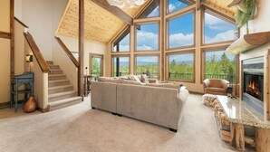 A spacious living room with a large sectional sofa, a fireplace, and a view of the outdoors through large windows. - Mountain Home on 10-Acres (Fraser)