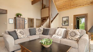 A living room with a sectional sofa, a coffee table with a plant, and a staircase leading to an upper level. - Mountain Home on 10-Acres (Fraser)