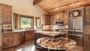 A spacious kitchen with wooden cabinets, granite countertops, a large island, and a stainless steel refrigerator. - Mountain Home on 10-Acres (Fraser)